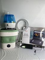 Photo showing portable washing machine with green collapsible body, humidifier with blue tank, circular Halo grow light, and boxed 13.3 inch portable DVD player.