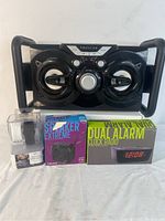Four items photographed together: large Proscan Bluetooth speaker, small boxed Speaker Extreme portable Bluetooth speaker, boxed Dual Alarm Clock Radio, and Bluetooth smart watch with two wrist straps and charger.