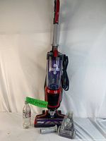 Front view of Dirt Devil Razor Pet upright vacuum standing upright with a Diet Coke bottle placed beside for size reference. Red and black color with translucent purple dust container.
