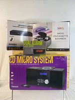 Boxes of Proscan HDMI Upconvert DVD Player with Dual Alarm Clock Radio, Radio CD/Cassette Boombox, and CD Micro System Bluetooth.