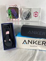 Overview of lot including pedometer watch in box, Anker Bluetooth speaker with box, MP3 player in white with earphones and cables, and Nintendo Switch Joy-Con controllers in packaging.