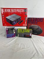 Full view of all four boxed items in the lot: Projector, CD Radio Boombox, Speaker Extreme, Dual Alarm Clock Radio.