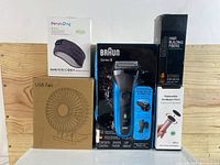 Full lot photo featuring all items: Braun face shaver, sleep headphones and eye mask, USB fan, sandpaper discs, hair building fibers box.