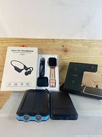 Photo of the whole lot showing pink smart watch in box with charger, two power banks, 3-in-1 wireless charger base, and box of Open Ear Headphones.