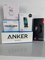 Photo of all items in the lot together including smart watch, wireless earbuds box, phone wall charger boxes, iWalk docking battery box, and Anker SoundCore speaker box.