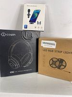 Black Cowin SE7 ANC wireless headphones box with images and LED RGB strip light box alongside wireless lavalier microphone box on top.