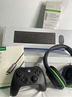 The wireless keyboard and mouse set box, wired Xbox controller, gaming headphones, USB-C to HDMI cable box, and outlet plug with surge protection box arranged together.