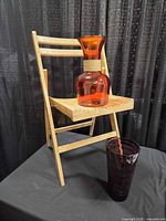 Orange glass vase on wooden folding chair, purple vase in front