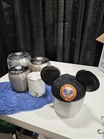 Overall view of three Kromex canisters, milk glass jar and Disneyland Mickey Mouse hat