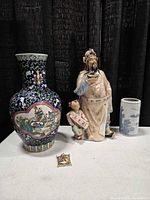 Group shot showing large colourful vase, figurine with child, small blue-white vase, and brooch on table