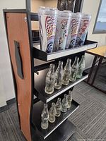 Side view of display shelf showing tumblers on top shelf and two rows of glass bottles