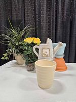 Group shot of faux plant arrangements, watering can, and ceramic planters on table