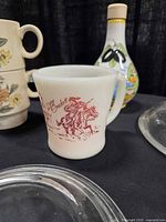 Close-up of Fire-King Davy Crockett mug with olive oil bottle and stacking mugs behind