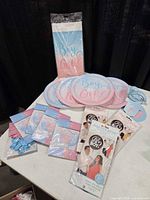 All items laid out: paper plates, latex balloon packs, gender reveal balloons, tablecloth