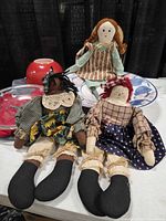 Overview of three rag dolls, red Fire-King bowl, ceramic fruit bowl, Pyrex pie plate
