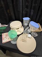 Overview of assorted Tupperware pieces, placemats, recipe book, glassware and stoneware on table