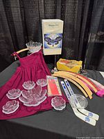 Lot overview showing glass bowls, dress, sports items, cookie press box, hangers, latch hook kit, house hippo
