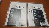 Two packaged GRA certificate cards with moissanite earrings displayed beside them