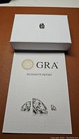 Photo showing the moissanite gemstone on a white box with GRA Moissanite authenticity report beneath it