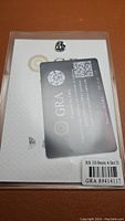 Top-down view of the loose moissanite stone alongside GRA certificate card showing RS 10.0mm 4.0ct D and serial number