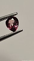 Pear-shaped pink-orange sapphire held by tweezers