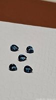 Five pear-shaped London blue topaz gemstones on a light surface, showing their rich blue hues and clarity.