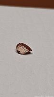 Pear-shaped padparadscha sapphire on white background, angled view