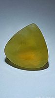 Close-up image of triangular, pear teardrop shaped yellow fire opal gemstone on white background showing translucency and facet surfaces.