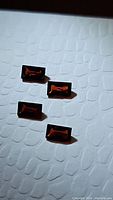 Four rectangular baguette cut orange red almandine garnet gemstones placed on white textured background.
