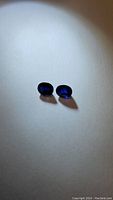 Two oval deep blue sapphires displayed on white surface under light