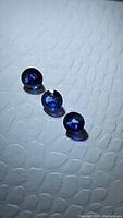 Three small, round, deep blue Ceylon sapphires arranged in a line on textured white surface, showing overall size and cut style.