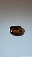 Photo of the octagon cut tourmaline showing the full face of the gemstone on a gray surface with light reflections revealing fanta orange-yellow color.