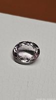 Light pink amethyst gemstone oval cut shown from above on a white textured background, highlighting its cut and clarity.