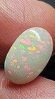Close-up image of an oval 4.45ct Ethiopian opal with multicolor flashes against a fingertip for scale.