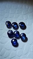 Seven round cabochon cut natural sapphire gemstones, displaying rich royal blue color and clarity, arranged on textured white background.