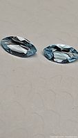 Two natural sky blue topaz gemstones, marquis cut, lying side by side on a surface, showing their clear sky blue color and facet pattern.