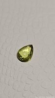 Pear shaped yellow-green faceted sphene gemstone lying on textured grey background showing overall color and cut shape.
