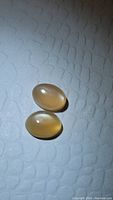 Pair of two oval polished cabochon peach moonstones laying on textured white surface showing their color and moonstone flash.