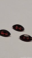Three marquise cut red-orange Pyrope garnet stones on a plain background, showing facets and clarity.