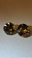 Photo of two round faceted sphene gemstones showing green-yellow color and strong shine.