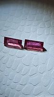 Close-up of two red-pink natural untreated ruby baguette cut gemstones on textured white background, showing facet details and natural inclusions.
