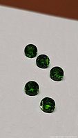Five round, electric green Russian chrome diopside gemstones on white textured background, medium lighting.