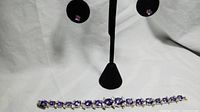 Front view of 10k gold amethyst earrings worn on display with silver-tone amethyst and accent stone bracelet displayed below.