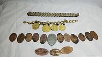 Full view of two bracelets and a collection of vintage souvenir smashed coins arranged in a row on a white background.