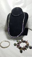 Showcase of the amethyst and sterling necklace on black bust along with the sterling silver round ball bracelet and the glass bead charm bracelet.