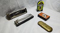 Group photo showing two harmonicas and three lighters: Marine Band M. Kohner harmonica, silver Hohner Marine Band harmonica, brass collectible lighter, Denver Broncos lighter, and jukebox lighter.