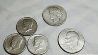 Set of six coins displayed on a light background showing one Peace dollar, one Eisenhower dollar, and four Kennedy half dollars.