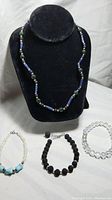 Photo showing four bracelets including lapis lazuli, azurite, pearl, turquoise, lava stone, and clear crystal beads displayed on a black jewelry bust and flat surface.