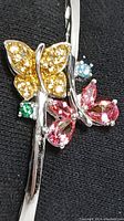 Close-up image of bracelet showing yellow and pink butterfly designs with colored stones and part of silver band.