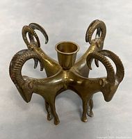 Front and side view of antique brass ram candleholder showing four ram heads with curved horns and central candle cup.